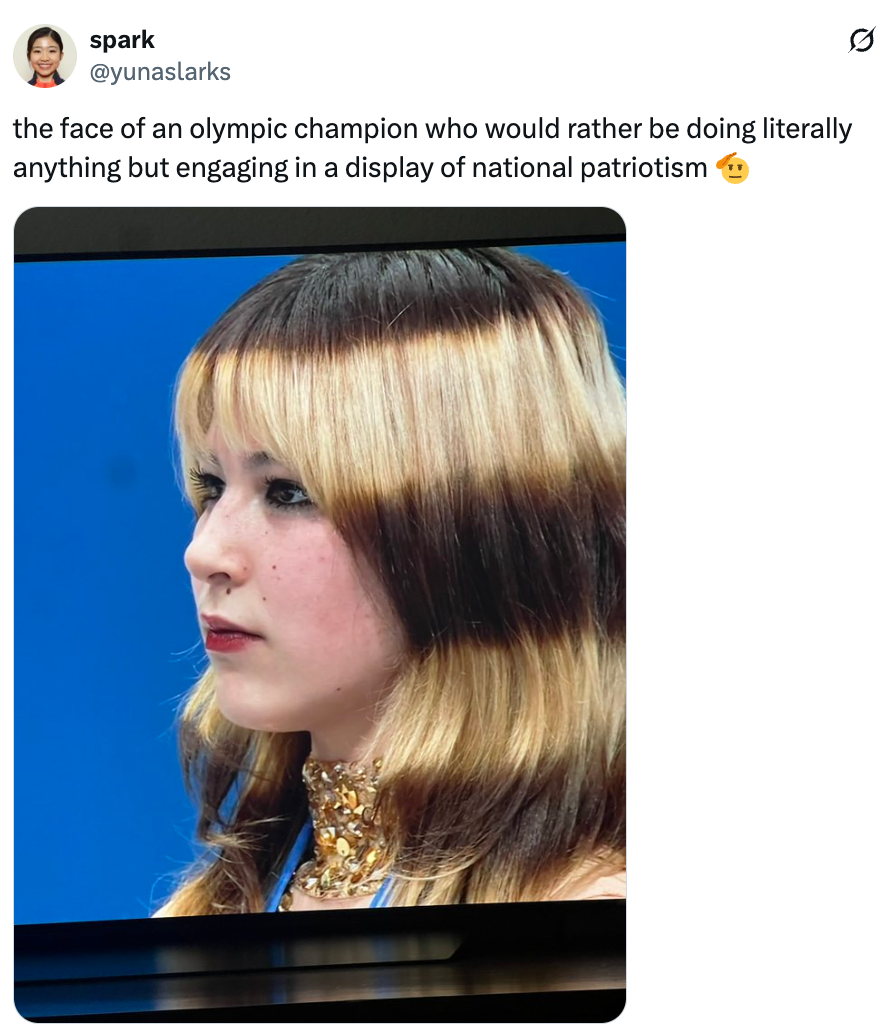 Person som ser uinteressert ut under en olympisk begivenhet, med langt hår og iført et halskjede