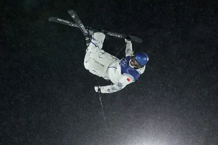 En skiløper i luften som utfører en flip under en nattlig begivenhet, iført hjelm og verneutstyr