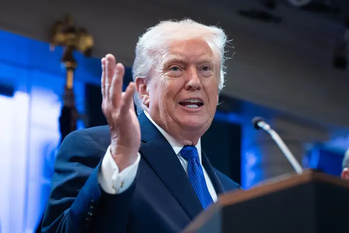 En person i dress gestikulerer mens han snakker ved et podium under en formell begivenhet