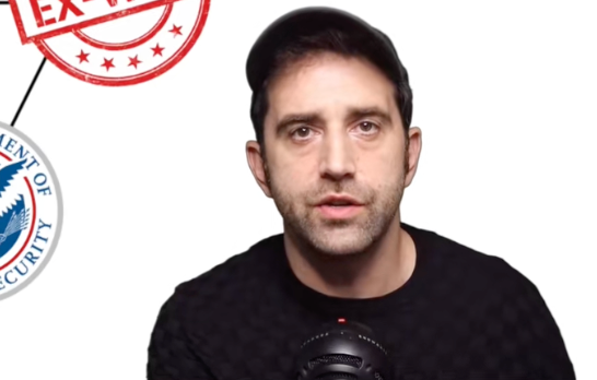 Mann i fritidsklær snakker inn i en mikrofon; offisielt segl delvis synlig i bakgrunnen