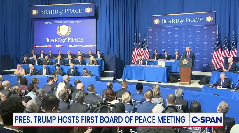President Trump taler ved et podium under et styremøte for fred, med et stort publikum og paneldeltakere på scenen. Flagg og skilting omgir arrangementet