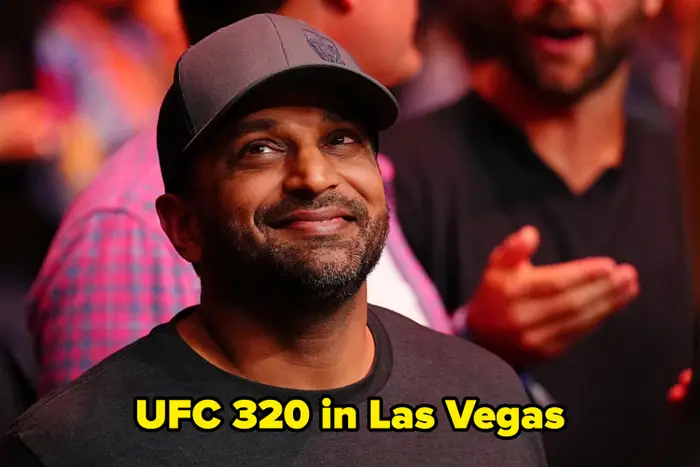 En person med caps og t-skjorte smiler i en folkemengde, med folk som snakker i bakgrunnen