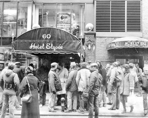 Folk som står i kø utenfor Hotel Elysée under en markise, med Monkey Bar-inngang i nærheten. Travelt gatebilde