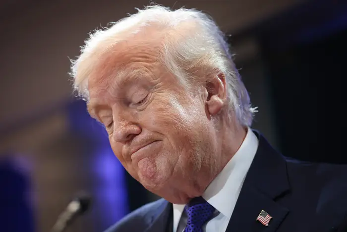 En person i dress på en nyhetshendelse ser ut til å lukke øynene og rynke litt på pannen mens han ser ned. En amerikansk flaggnål er på jakkeslaget deres