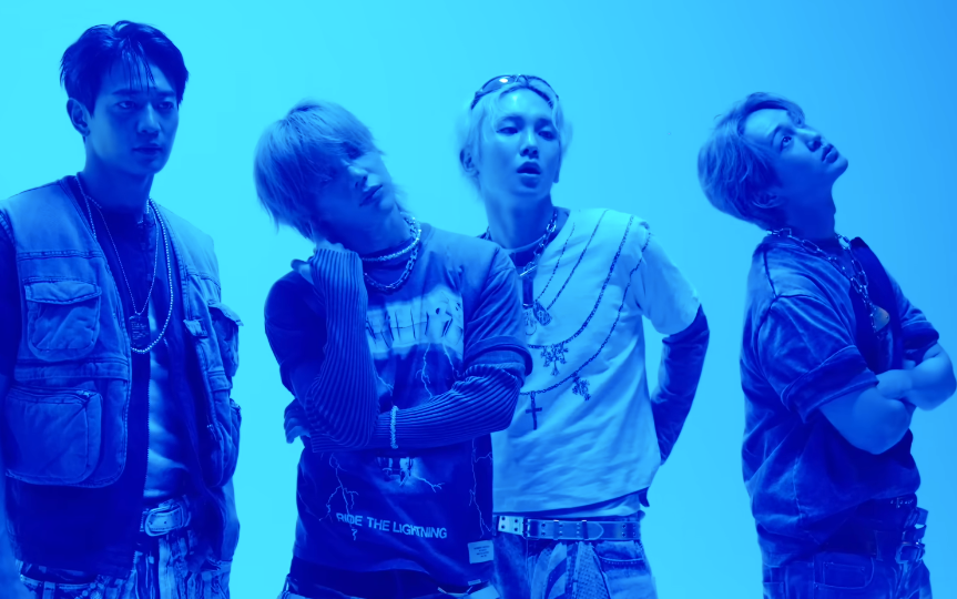 Fire personer poserer selvsikkert i lagdelt streetwear, med grafiske skjorter og smykker, mot et vanlig bakteppe