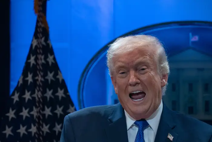 Person i dress som snakker energisk på scenen med flagg og emblem synlig i bakgrunnen