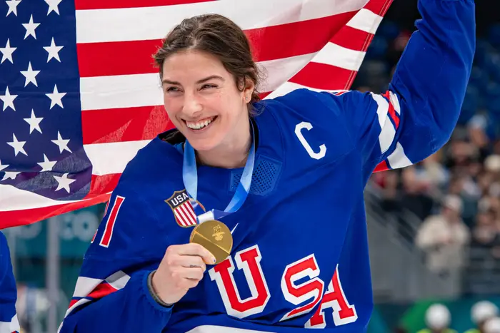 Atlet holder en medalje, smilende, drapert i et amerikansk flagg. Bærer en USA-hockeytrøye med en kapteins 