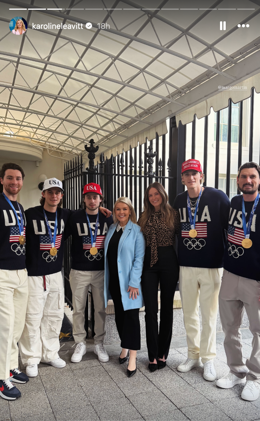 En gruppe mennesker poserer under en overbygd gangvei. Flere har på seg OL-gensere og medaljer med USA-tema. En kvinne i lett frakk står i midten