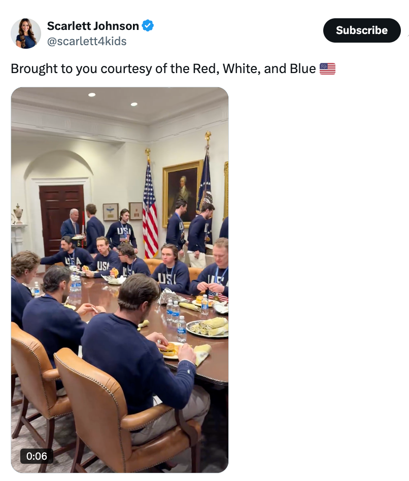 Gruppe mennesker i marinen "USA" gensere som sitter rundt et bord og spiser, med amerikanske flagg synlige i bakgrunnen