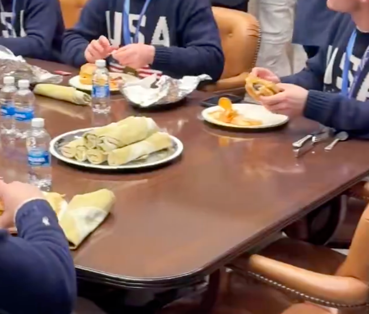 Folk satt rundt et bord og spiste hurtigmat med burritos og flaskevann. De har på seg gensere med "USA" på dem