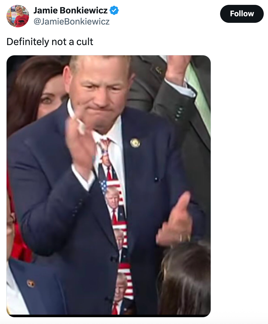En mann i dress klapper, iført et slips med trykte Trump-ansikter. Tweeten over ham lyder: "Definitivt ikke en kult."