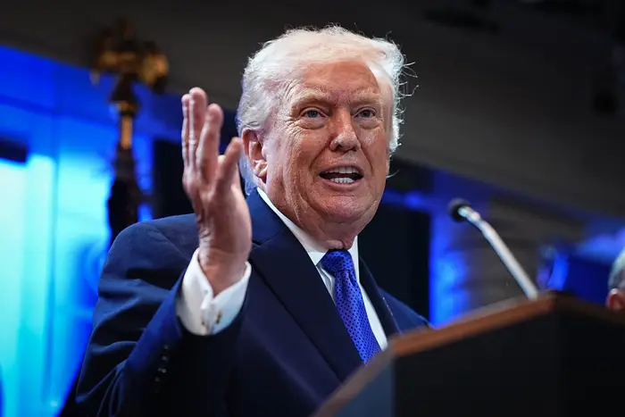 Donald Trump ved et podium, gestikulerer med én hånd, med et nøytralt uttrykk i en formell setting