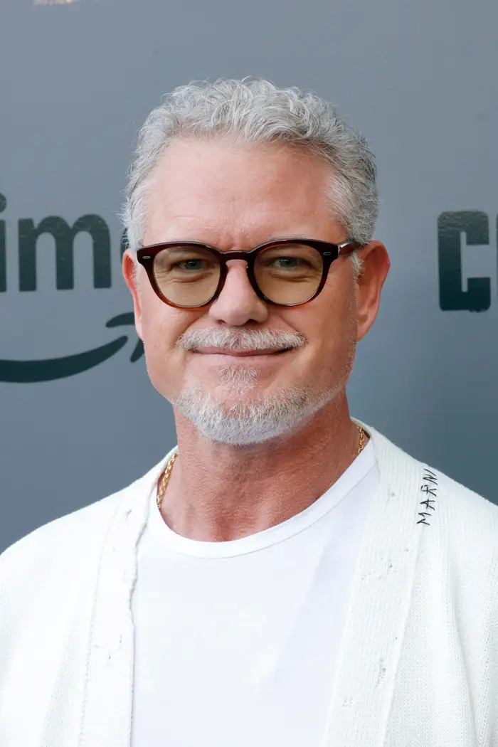 Mann med kort grått hår, briller, hvitt skjegg iført en hvit skjorte og jakke på et kjendisarrangement