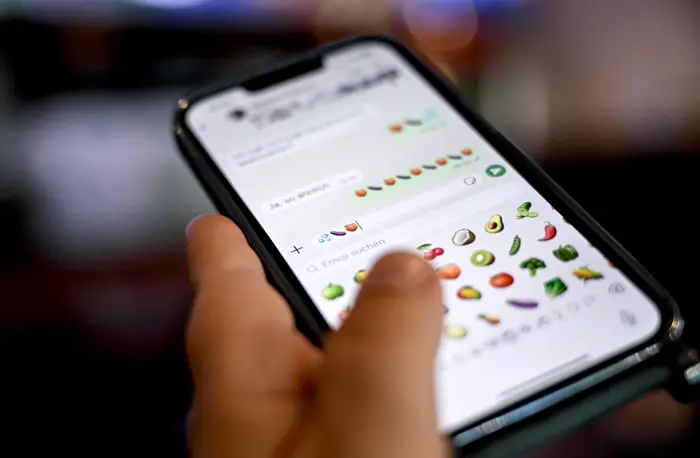 Person som bruker en smarttelefon og blar gjennom en rekke frukt-emojier i en meldingsapp