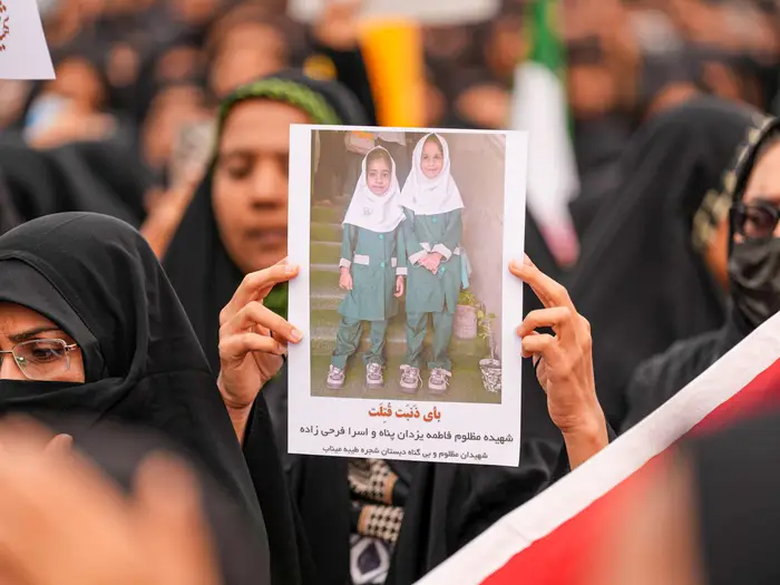 Person holder et bilde av to smilende barn i matchende antrekk under en offentlig sammenkomst