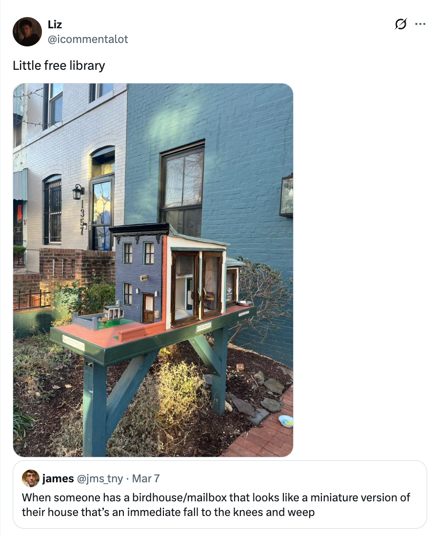 Minikopi av et hus brukt som gratis bibliotek sitter på en trestativ utenfor en bygning