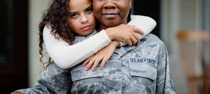 Barn som omfavner en person i en US Air Force-uniform, står utenfor med ballonger i bakgrunnen