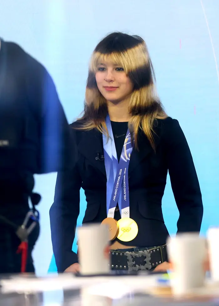 Kjendis iført en skreddersydd dress med gullmedaljer rundt halsen, stående på en scene