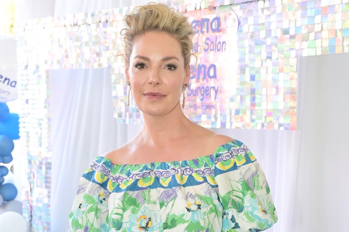 Person i blomstret off-the-skulder kjole på et salongarrangement, stående foran et bakteppe med dekorative ballonger