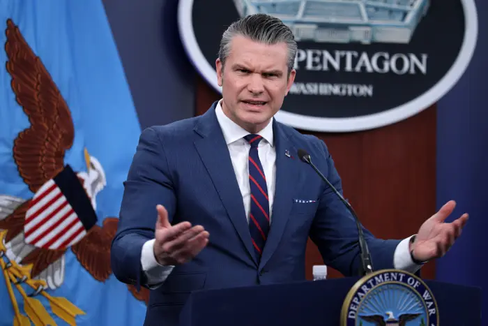 Pete Hegseth står på et podium med et Pentagon-emblem og gestikulerer mens han snakker på en pressekonferanse