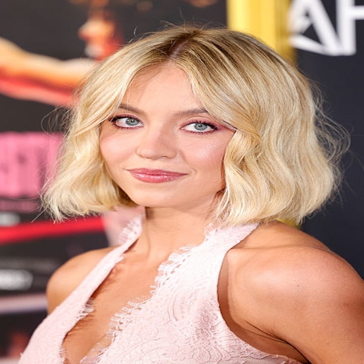 Person i en rosa blondekjole poserer på et arrangement, med en filmplakat i bakgrunnen