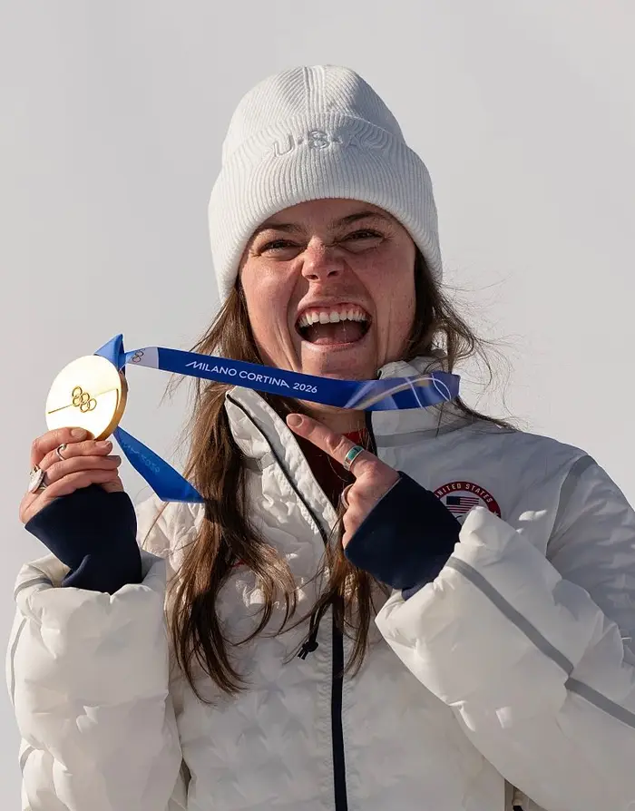 Person i uformelt vinterantrekk har en OL-gull i Milano Cortina i 2026, smilende begeistret