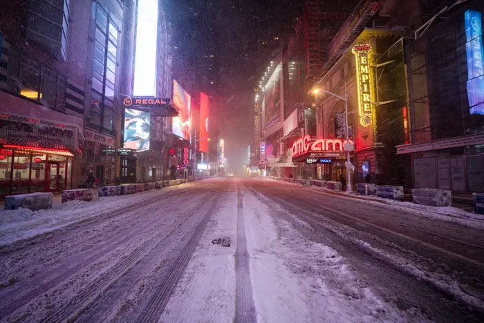 Snødekket Times Square-gate om natten, med lysende neonskilt og tomme fortau