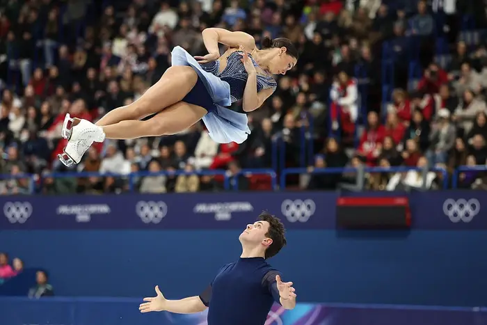 Kunstløpere utfører et dramatisk løft under en konkurranse, der den kvinnelige skateren svever grasiøst over partneren sin