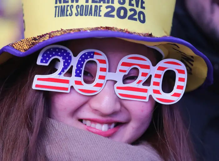 Person som har på seg "2020" briller med amerikansk flaggmønster på nyttårsaften Times Square-arrangement, smilende og iført en festlig hatt