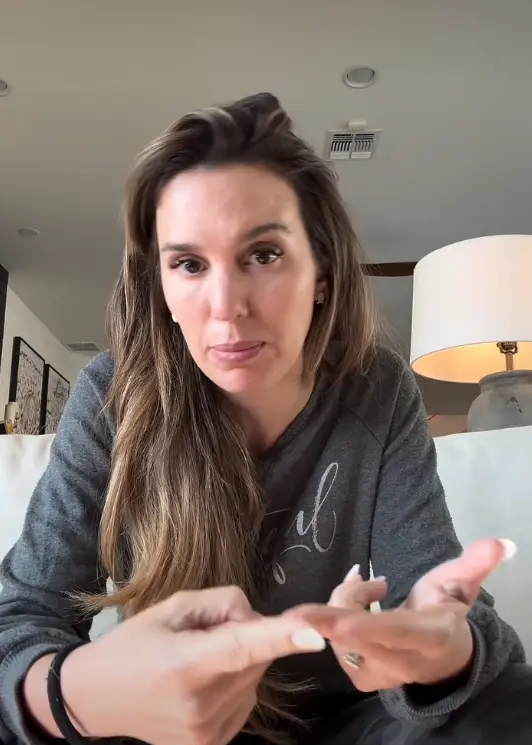 Person som sitter på en sofa, iført en uformell genser, gestikulerer med hendene. Innendørs setting med en lampe i bakgrunnen