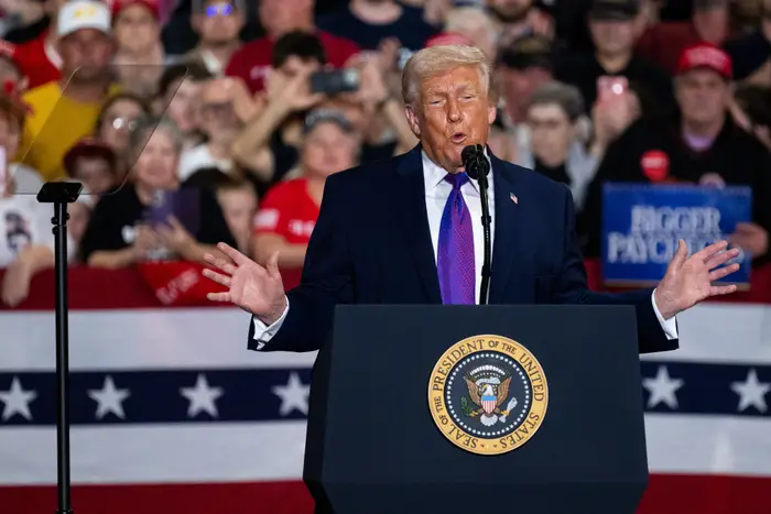Person som taler ved et podium med en presidentsegl, og taler til en folkemengde på et møte