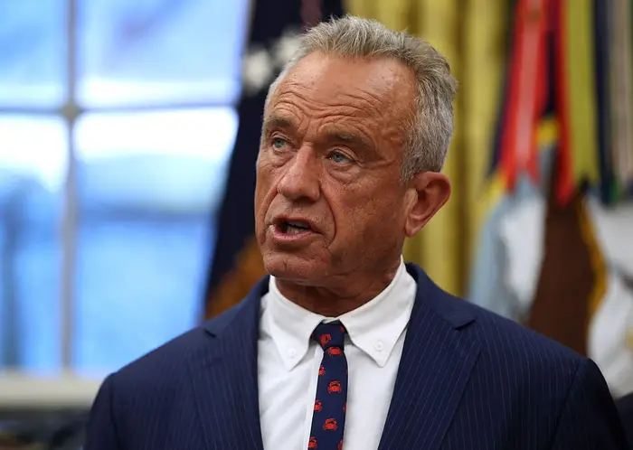 En person i dress og slips snakker i en innendørs setting, muligens leverer nyheter eller en uttalelse