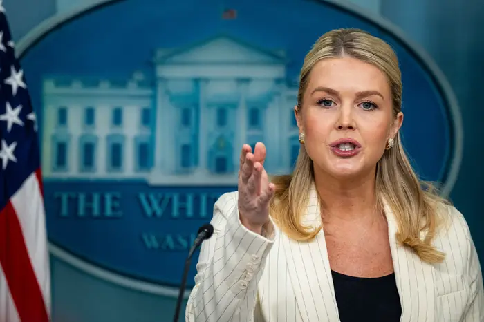 En person snakker lidenskapelig ved et podium med et emblem fra Det hvite hus i bakgrunnen, kledd i en nålestripet blazer