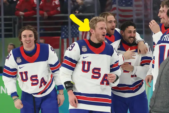 Hockeyspillere i USA-trøyer feirer på isen, smiler og omfavner hverandre. Et amerikansk flagg er synlig i bakgrunnen