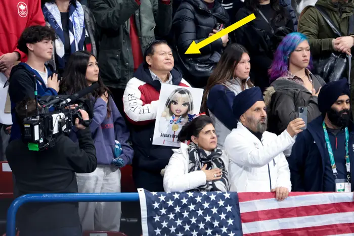 Tilskuere på et arrangement som fanger øyeblikk; en person holder et skilt med en tegneseriefigur. Et amerikansk flagg er drapert i forgrunnen