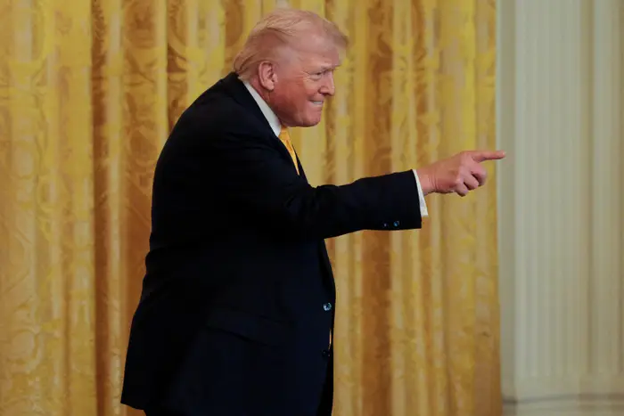 En person i dress peker og står foran et dekorativt gardin under et arrangement