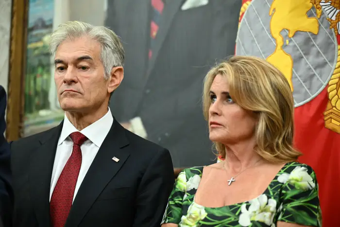 To individer står i formell antrekk; den ene har på seg en mørk dress med rødt slips, den andre en grønn blomsterkjole med et kors halskjede