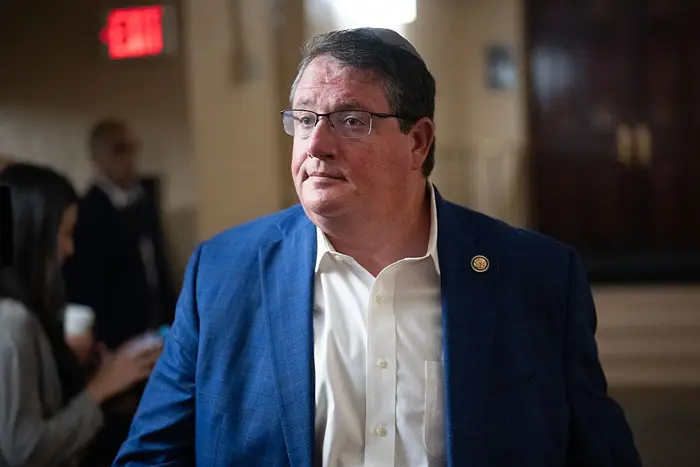 En person i blå blazer og hvit skjorte står i en gang og ser til siden. Andre er uskarpe i bakgrunnen