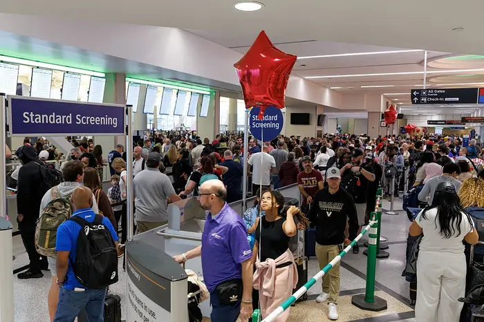 Overfylt sikkerhetslinje på flyplassen med folk som venter på å bli screenet. En rød ballong er i forgrunnen over linjen
