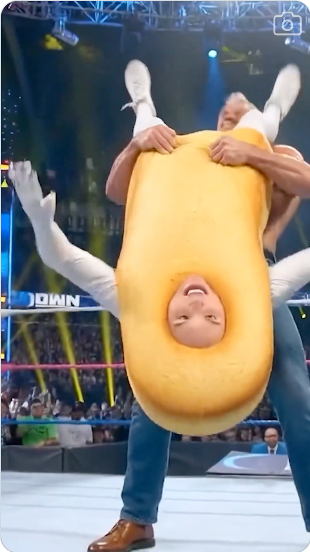 Brytekampøyeblikk: person iført et gult Twinkie-kostyme løftet av en annen bryter, fengslende publikum