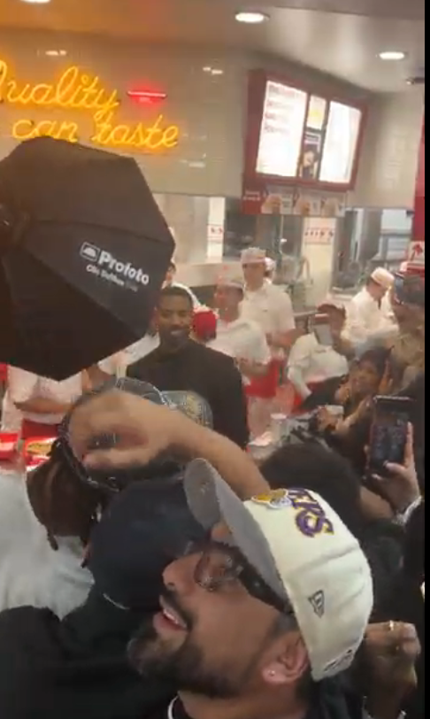 En folkemengde samles inne i en travel gatekjøkkenrestaurant, tar bilder og holder opp telefoner og fanger den travle scenen