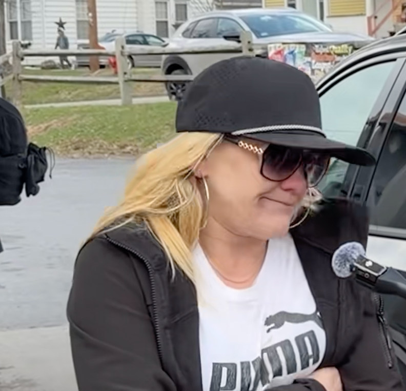 Person i uformelt antrekk og solbriller som snakker i en mikrofon utendørs