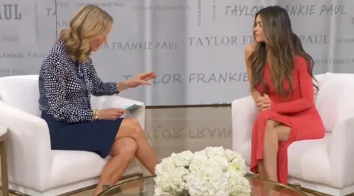 To kvinner sittende, engasjert i samtale under et intervju. Man har på seg en rød kjole; den andre er i mønstret bluse og blått skjørt