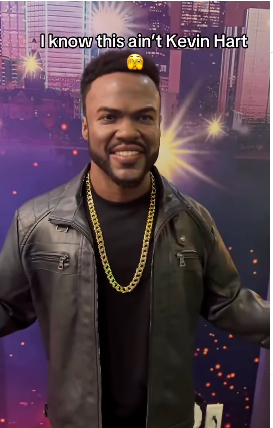 En mann i skinnjakke og gullkjede står og smiler. Bakgrunnen har innredning med bytema. Teksten ovenfor sier: 