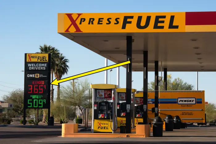 Bensinstasjon med prisskilt og Penske lastebil ved pumpe. Pris for vanlig gass oppført som $3,65. Ørkenlandskap i bakgrunnen