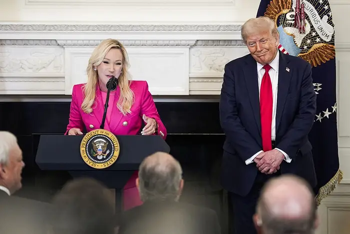 Jeg vet ikke hvem disse menneskene er, men kvinnen i et formelt antrekk taler ved et podium med en presidentsegl, mens en mann i dress står ved siden av henne