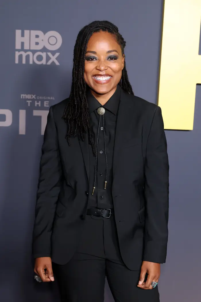 Person i svart dress med slips, smilende på en TV-seriepremierebegivenhet