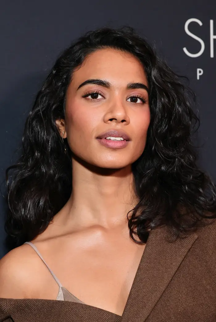 Person som poserer i et off-shoulder-antrekk på et arrangement, med hår stylet i løse bølger