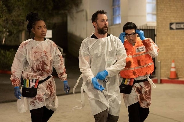 Tre personer, i verneutstyr sprutet med falskt blod, går i et filmmiljø, engasjert i en alvorlig samtale