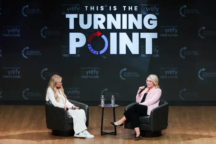 To personer har en samtale på scenen ved et Turning Point-arrangement, sittende i stoler med mikrofoner, foran et stort utstillingsskilt